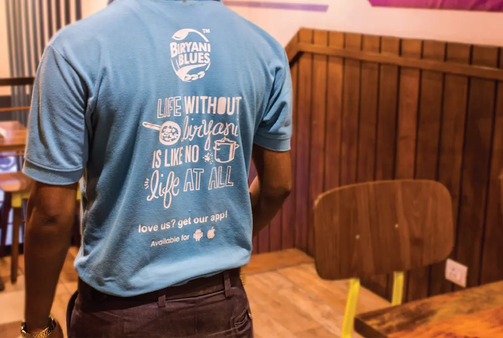 A man wearing a blue t - shirt standing in a restaurant.