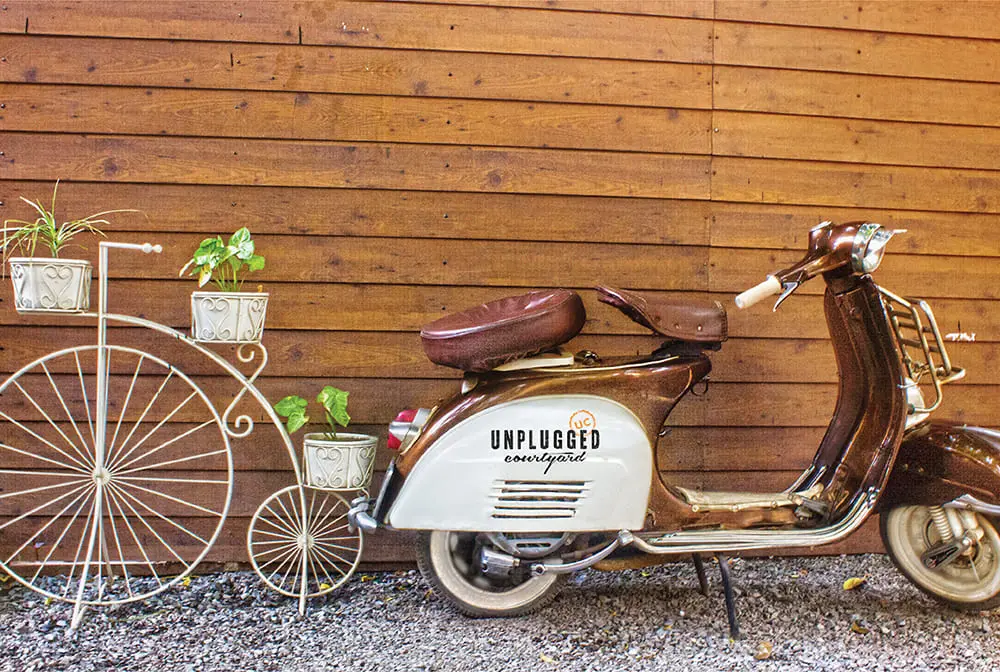 A vespa parked next to a wooden fence.