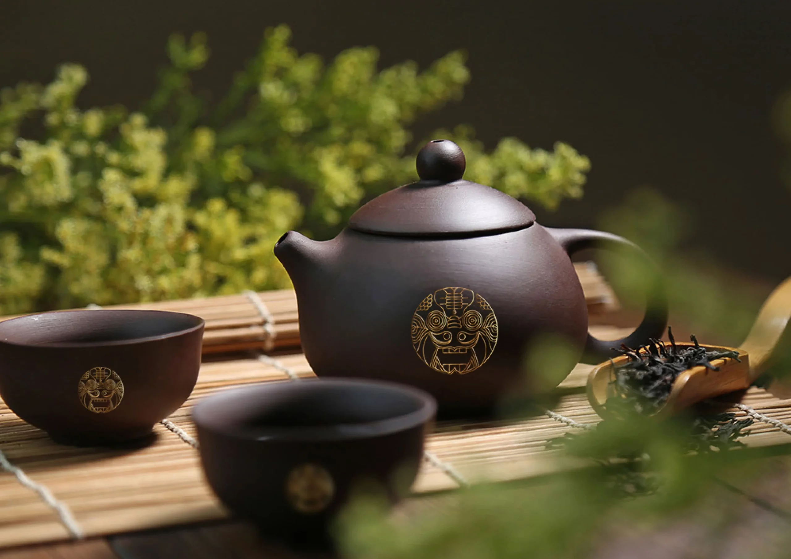 A tea set with two cups and a teapot on a bamboo mat.