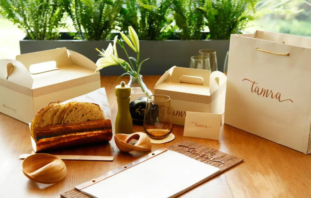 A wooden table with bread, bread boxes, and a notepad.