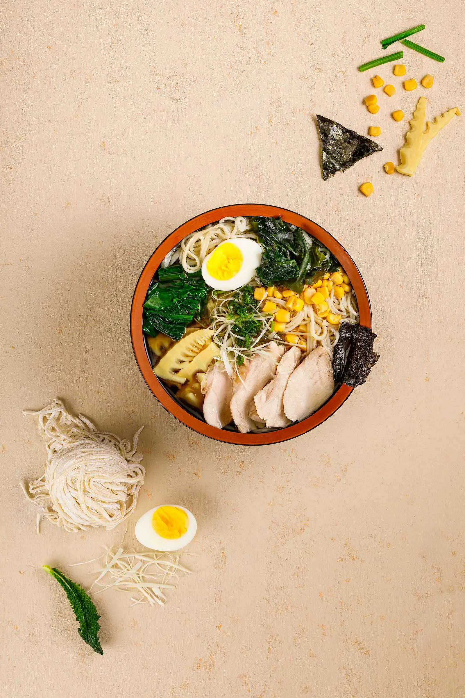 A bowl of ramen with eggs and vegetables on a beige background.