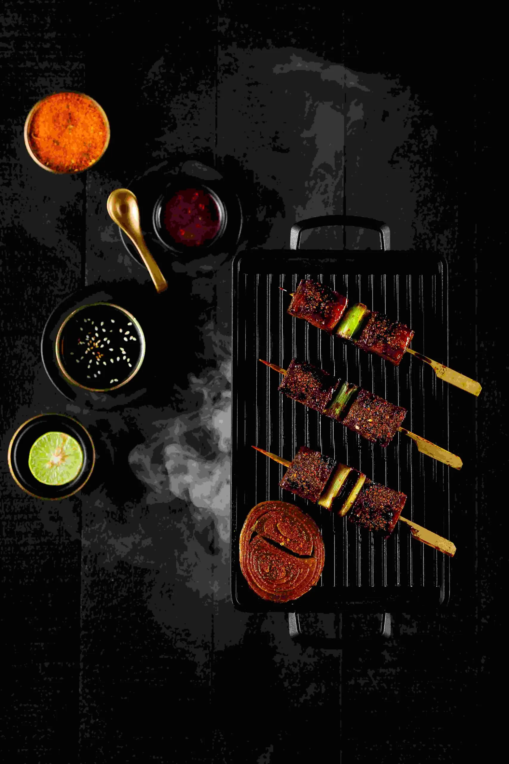 A grill with skewers and sauces on it.