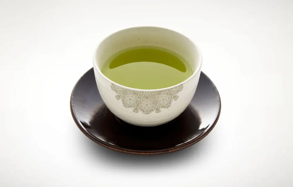 A cup of green tea sitting on a saucer.